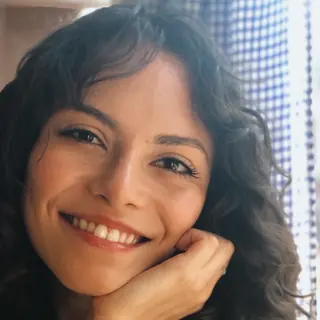 Mariana Calegari sorrindo, com a mão apoiada no rosto